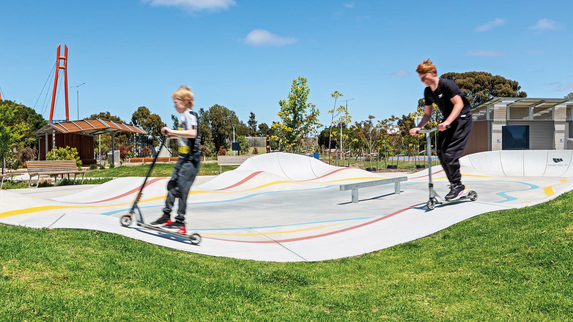Two children riding scooters on a precast concrete pump track from Parkitect Australia